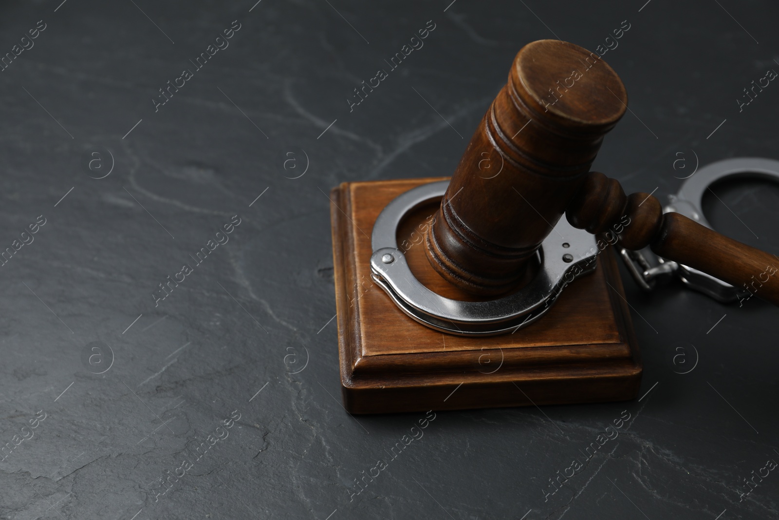 Photo of Handcuffs and judge's gavel on grey textured table, closeup. Space for text