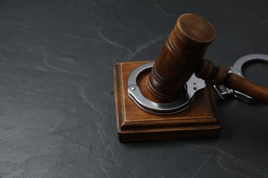 Handcuffs and judge's gavel on grey textured table, closeup. Space for text