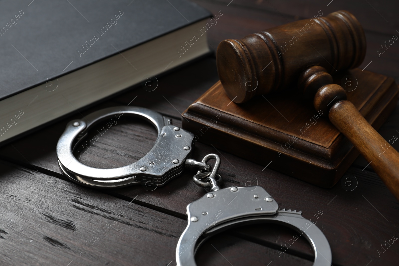 Photo of Handcuffs, judge's gavel and book on wooden table, closeup