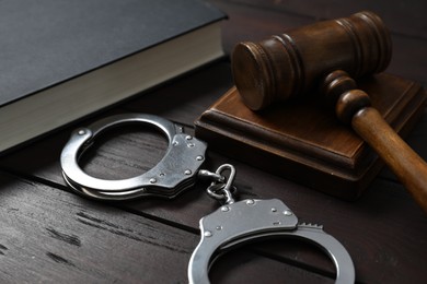 Photo of Handcuffs, judge's gavel and book on wooden table, closeup