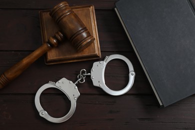 Photo of Handcuffs, judge's gavel and book on wooden table, flat lay