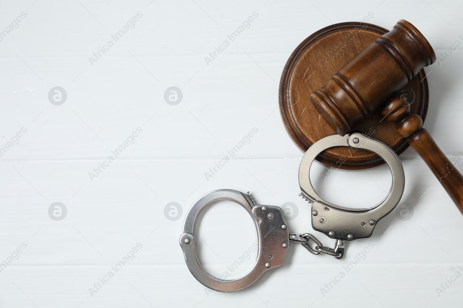 Photo of Handcuffs and judge's gavel on white wooden table, flat lay. Space for text