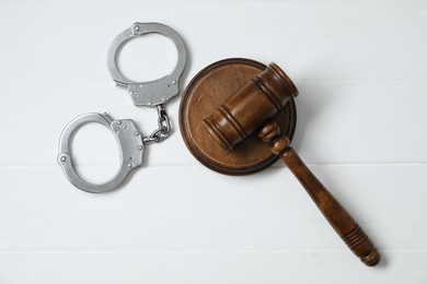 Handcuffs and judge's gavel on white wooden table, flat lay