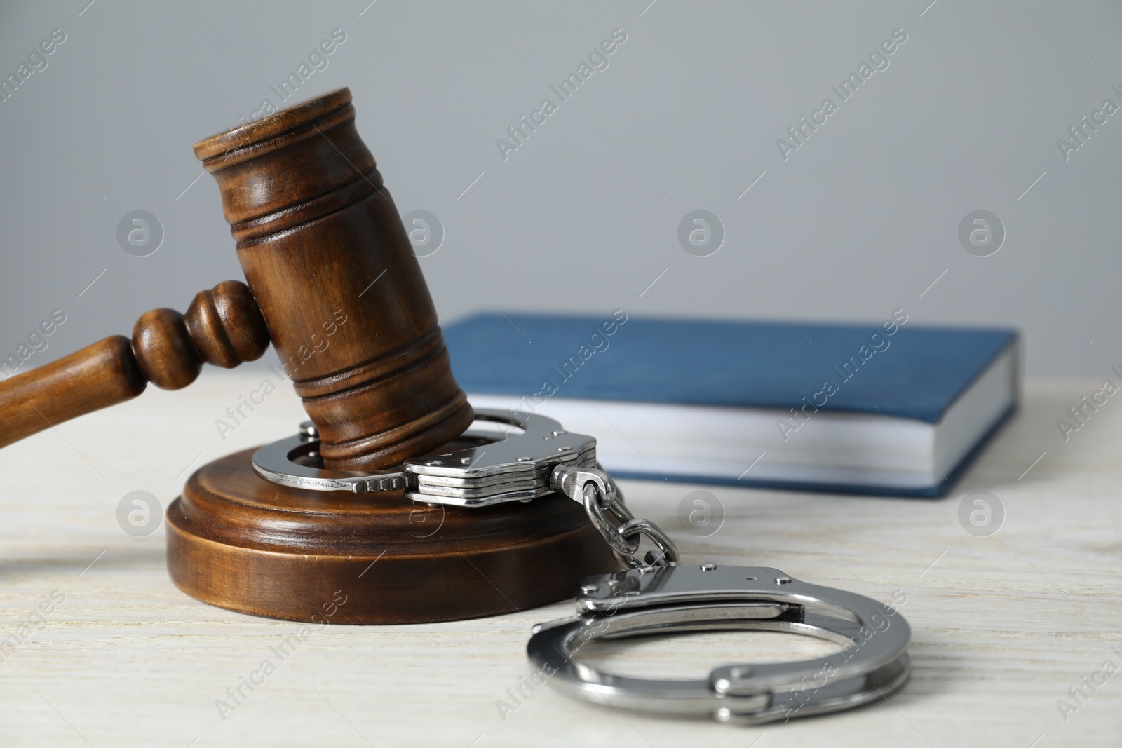 Photo of Handcuffs, judge's gavel and book on white wooden table, closeup