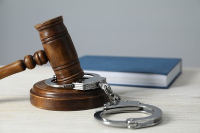 Handcuffs, judge's gavel and book on white wooden table, closeup