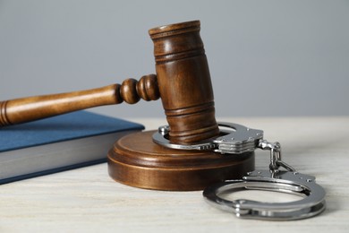 Photo of Handcuffs, judge's gavel and book on white wooden table, closeup