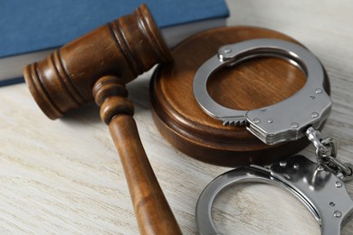 Handcuffs and judge's gavel on white wooden table, closeup