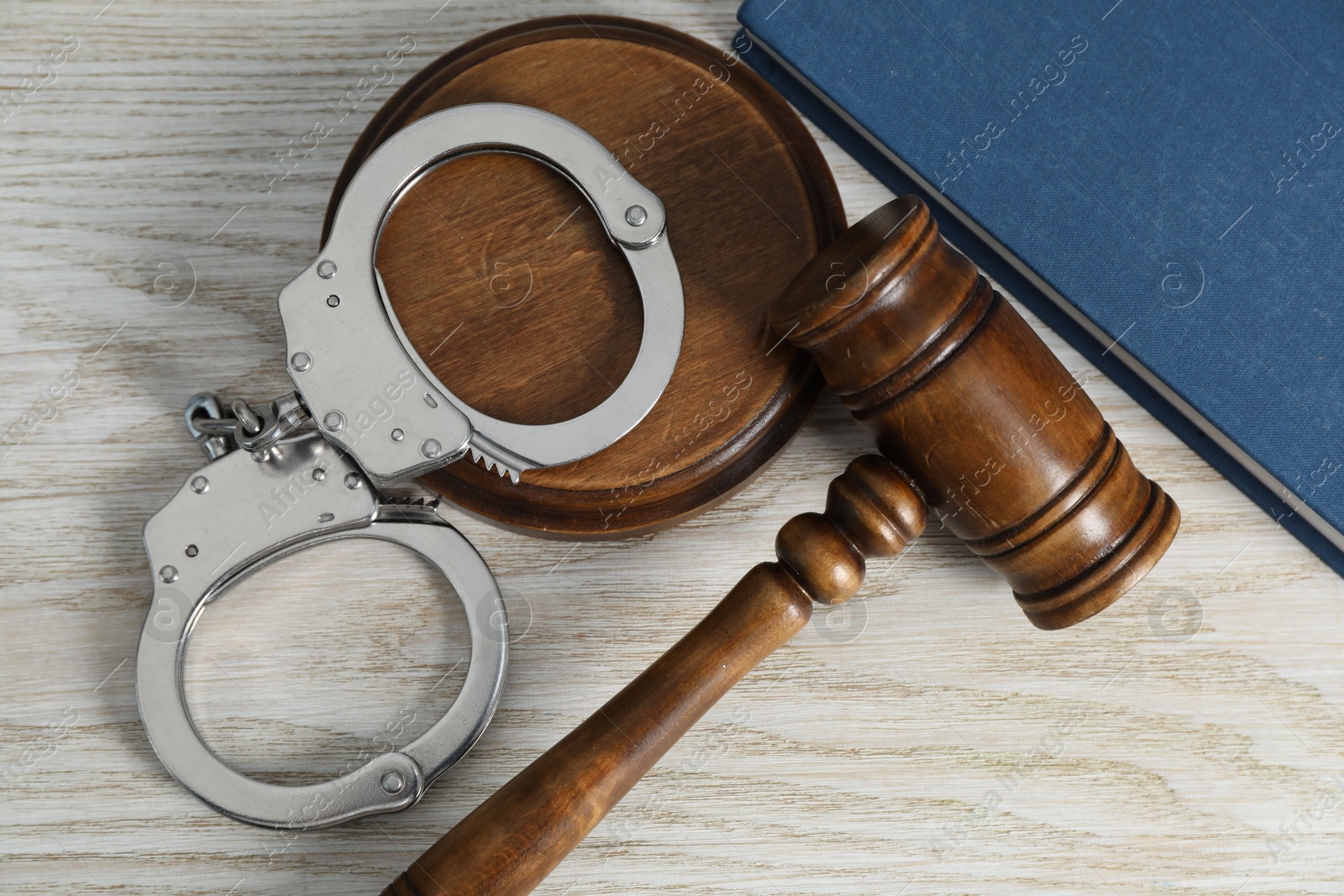 Photo of Handcuffs, judge's gavel and book on white wooden table, flat lay