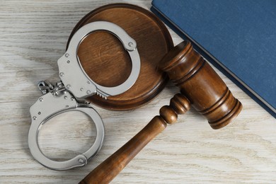 Handcuffs, judge's gavel and book on white wooden table, flat lay