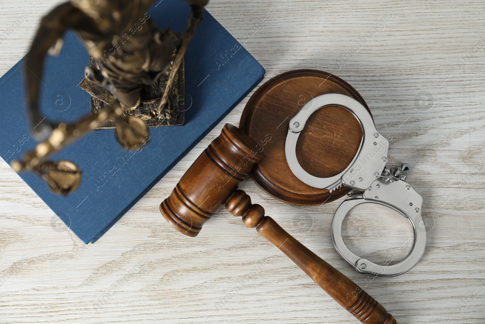 Photo of Handcuffs, judge's gavel, Lady Justice figure and book on white wooden table, flat lay