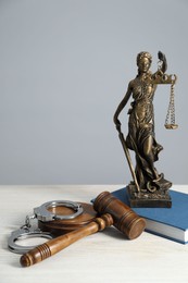 Handcuffs, judge's gavel, Lady Justice figure and book on white wooden table