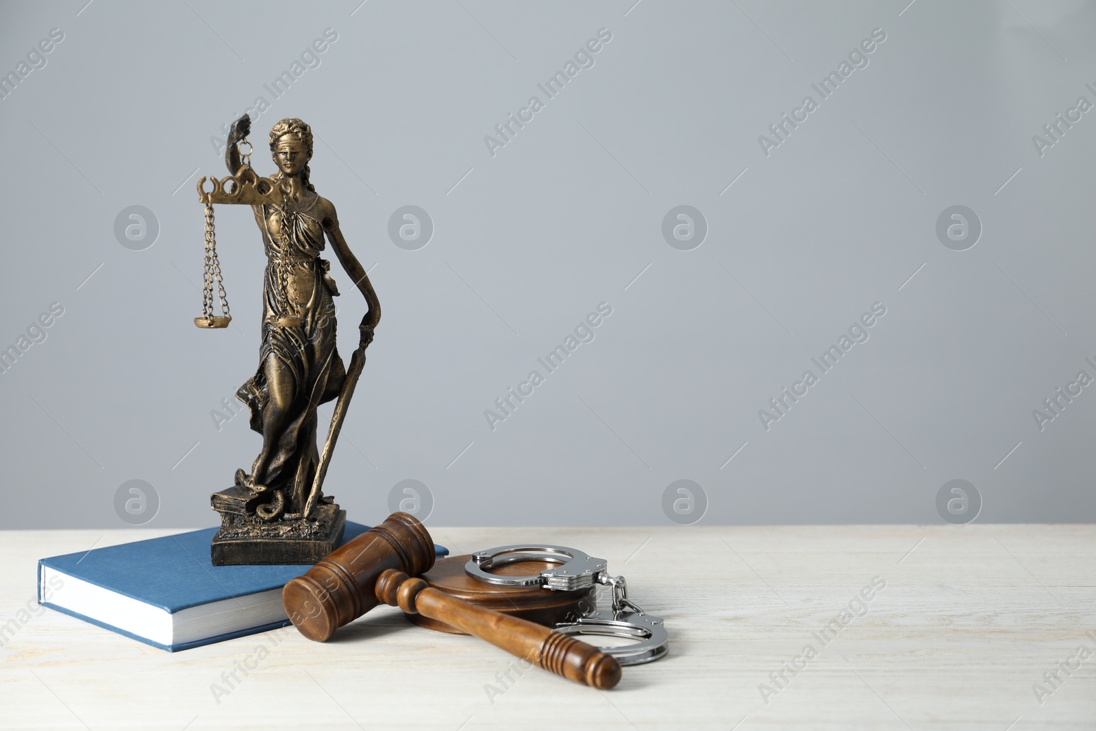 Photo of Handcuffs, judge's gavel, Lady Justice figure and book on white wooden table, space for text