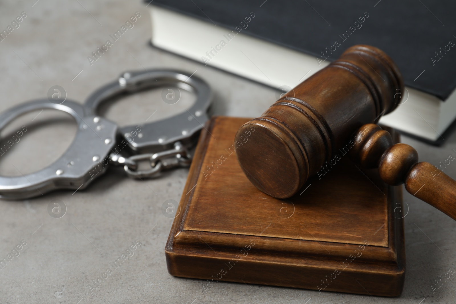 Photo of Handcuffs and judge's gavel on grey table, closeup