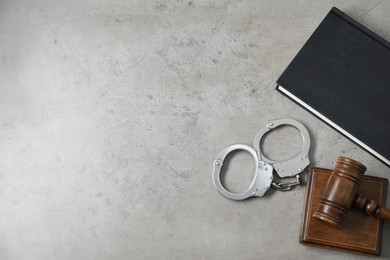 Handcuffs, judge's gavel and book on grey textured table, flat lay. Space for text