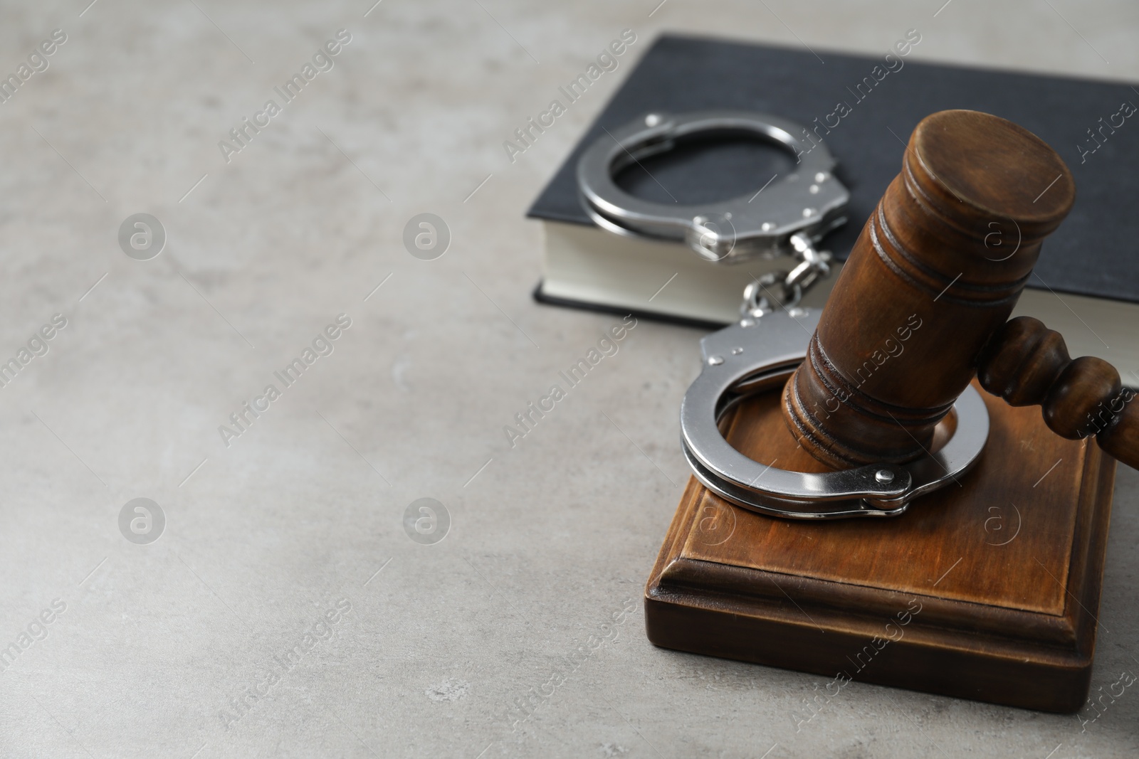 Photo of Handcuffs, judge's gavel and book on grey textured table, space for text