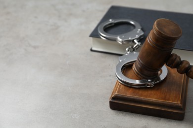 Handcuffs, judge's gavel and book on grey textured table, space for text