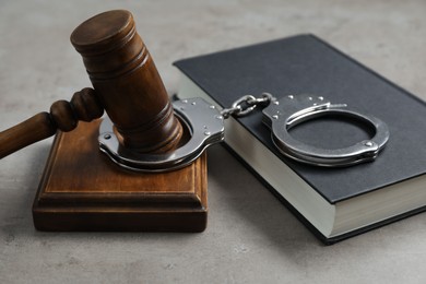 Photo of Handcuffs, judge's gavel and book on grey textured table, closeup