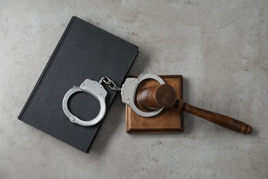 Handcuffs, judge's gavel and book on grey textured table, flat lay