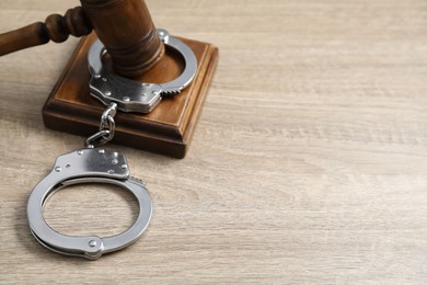 Handcuffs and judge's gavel on wooden table, space for text