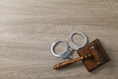 Handcuffs and judge's gavel on wooden table, flat lay. Space for text