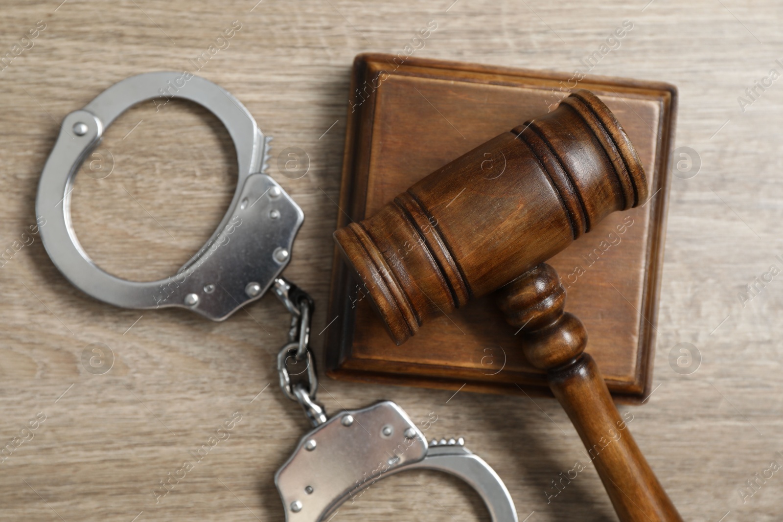 Photo of Handcuffs and judge's gavel on wooden table, flat lay