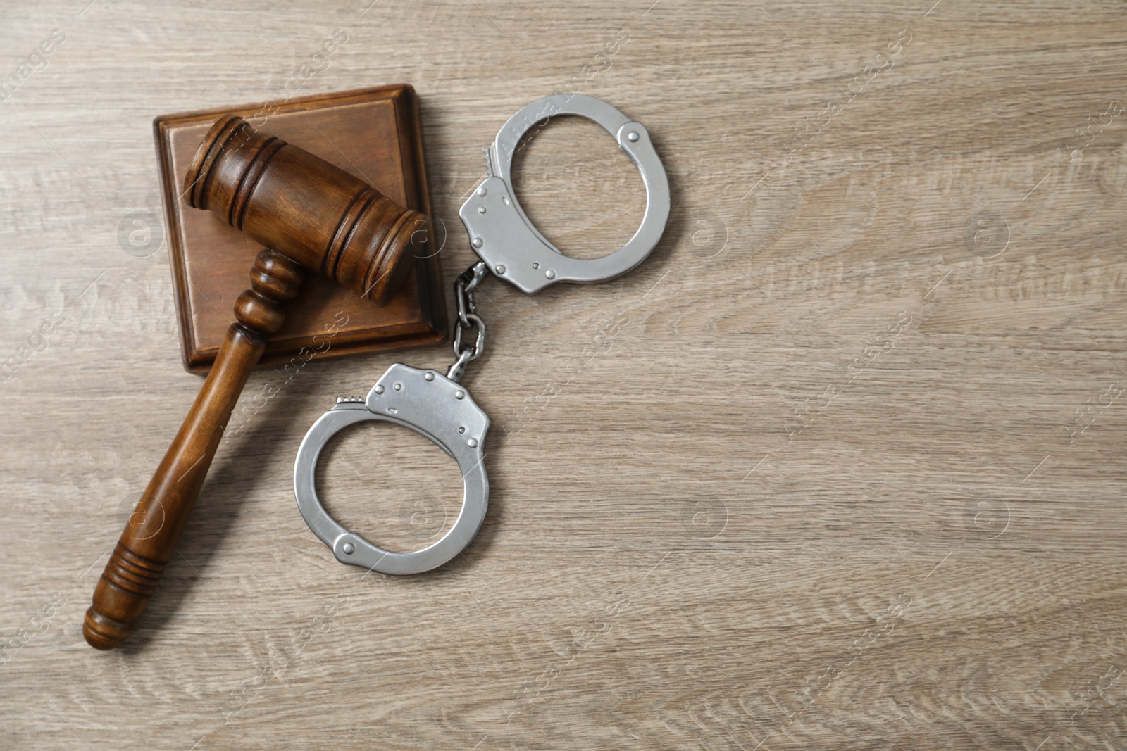 Photo of Handcuffs and judge's gavel on wooden table, flat lay. Space for text