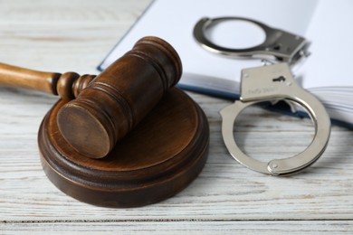 Handcuffs, judge's gavel and book on white wooden table, closeup