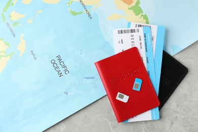 Photo of Passports, SIM cards, tickets and world map on grey marble table, flat lay