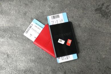 Passports with tickets and SIM cards on grey textured table, flat lay