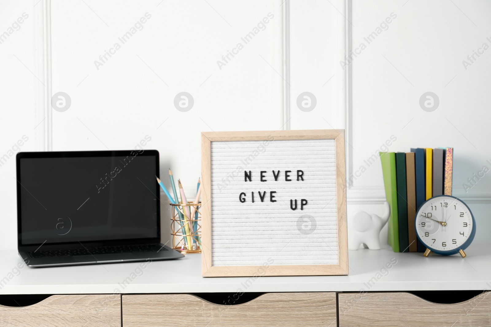 Photo of Letter board with phrase Never Give Up, laptop, alarm clock and stationery on white desk