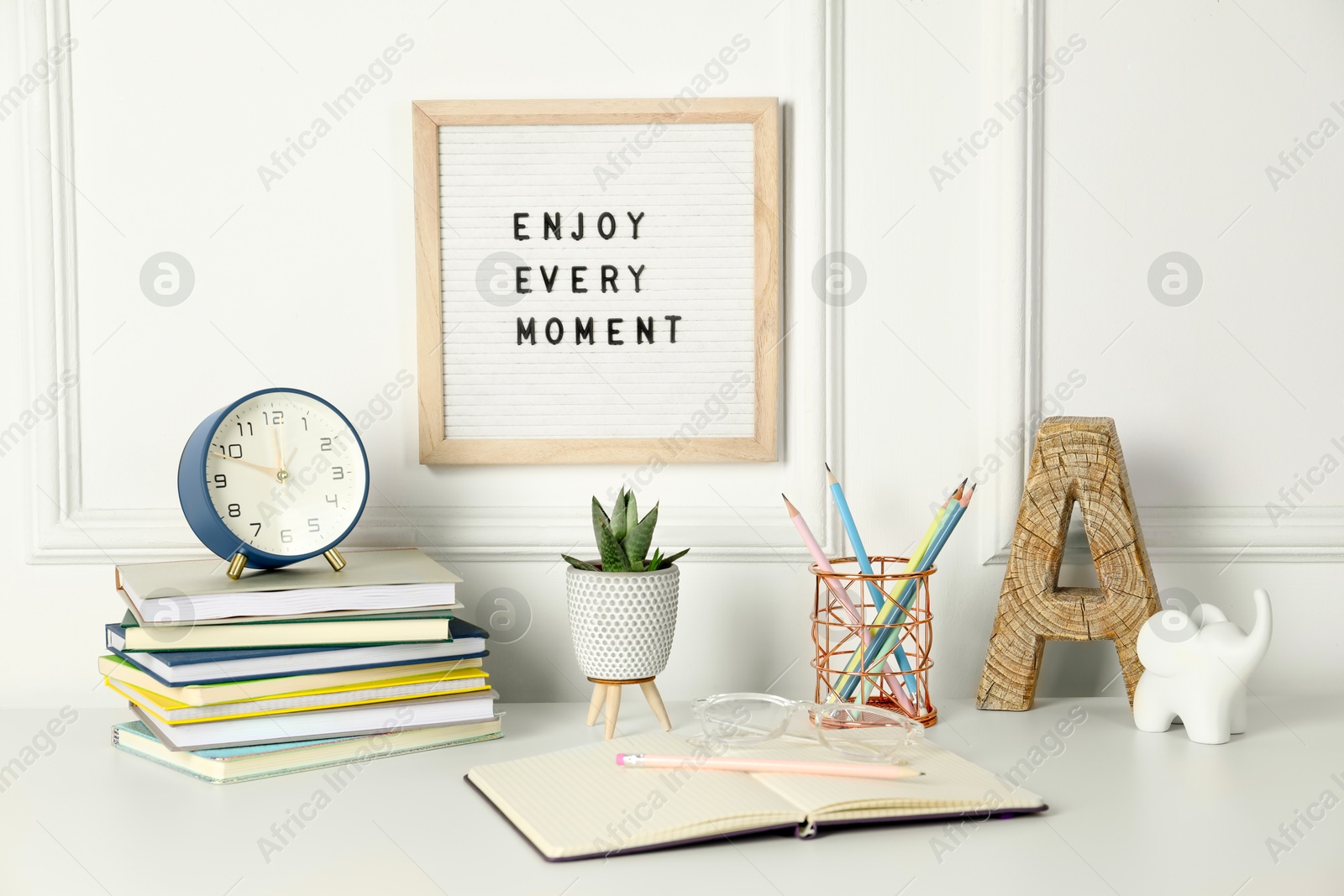 Photo of Letter board with phrase Enjoy Every Moment, alarm clock, decor and stationery on white desk