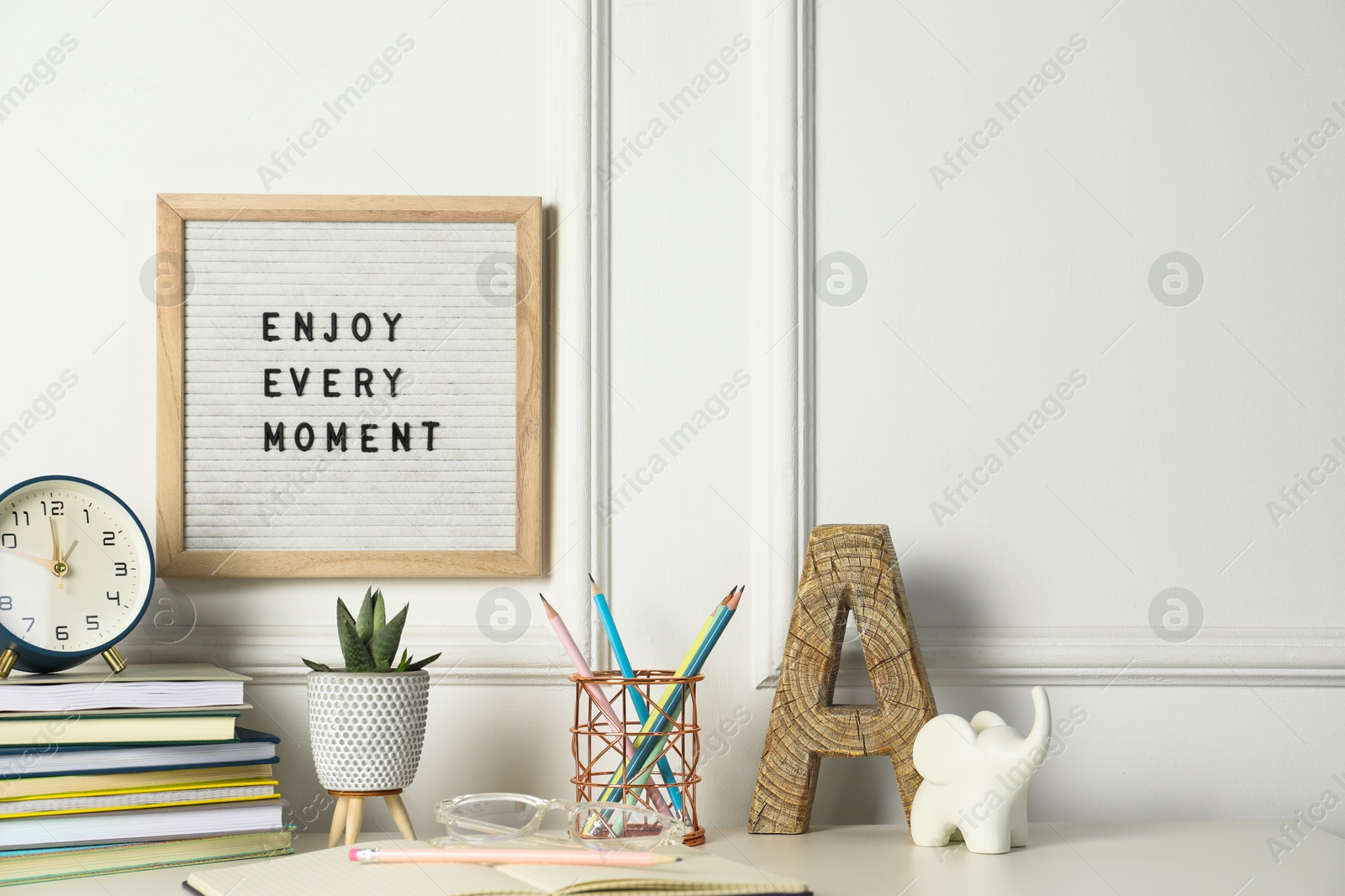 Photo of Letter board with phrase Enjoy Every Moment, alarm clock, decor and stationery on white desk