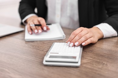 Photo of Banker with notebook using calculator at wooden table in office, closeup