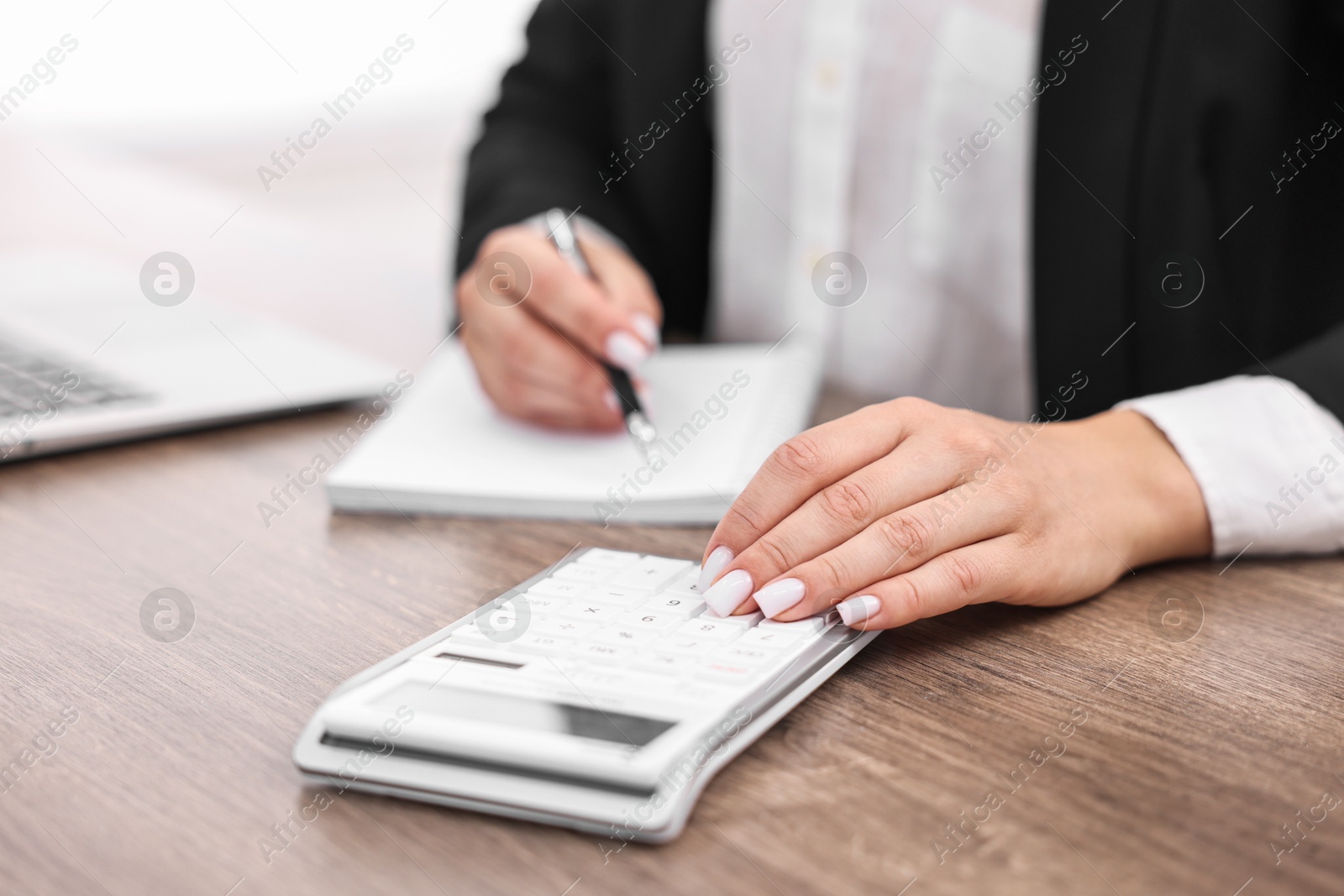 Photo of Banker with notebook using calculator at wooden table in office, closeup