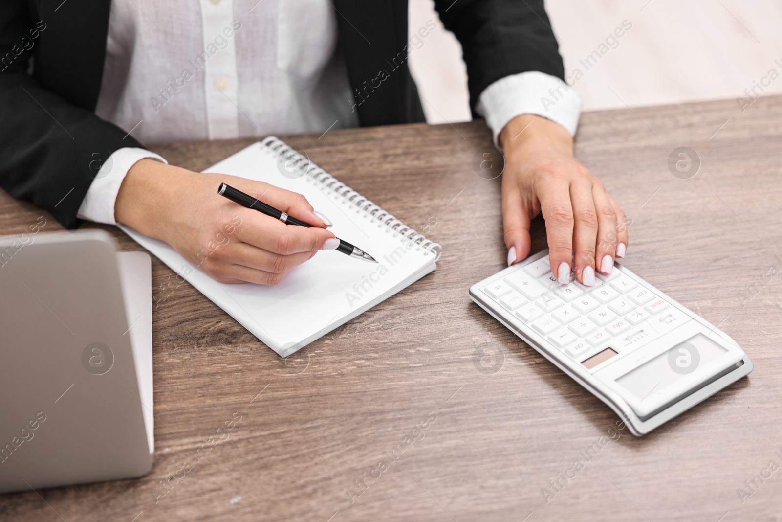 Photo of Banker with notebook using calculator at wooden table in office, closeup