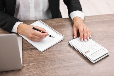 Photo of Banker with notebook using calculator at wooden table in office, closeup