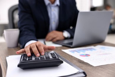 Photo of Banker using calculator at wooden table in office, closeup