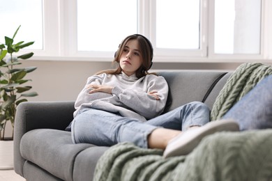 Loneliness concept. Sad teenage girl in headphones listening to music on sofa at home