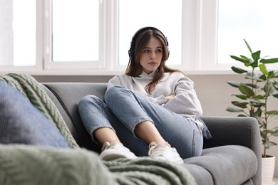 Photo of Loneliness concept. Sad teenage girl in headphones listening to music on sofa at home