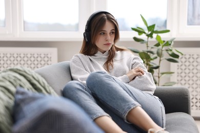 Photo of Loneliness concept. Sad teenage girl in headphones listening to music on sofa at home