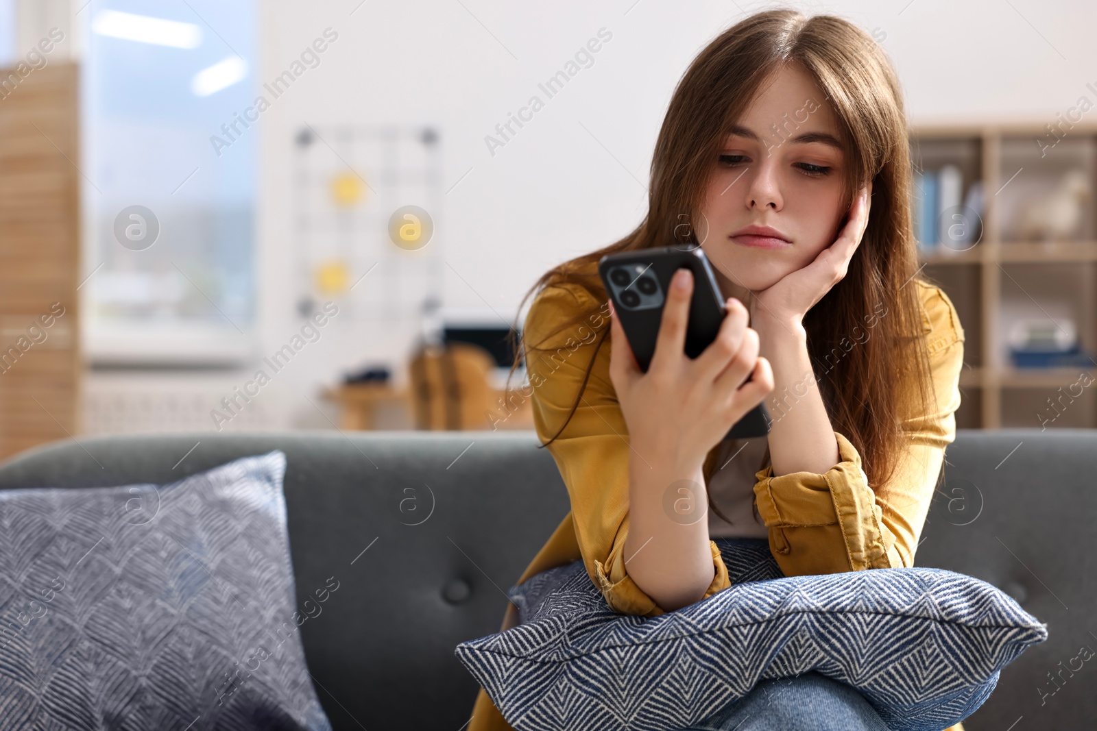 Photo of Loneliness concept. Sad teenage girl using smartphone on sofa at home