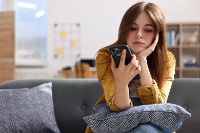 Loneliness concept. Sad teenage girl using smartphone on sofa at home