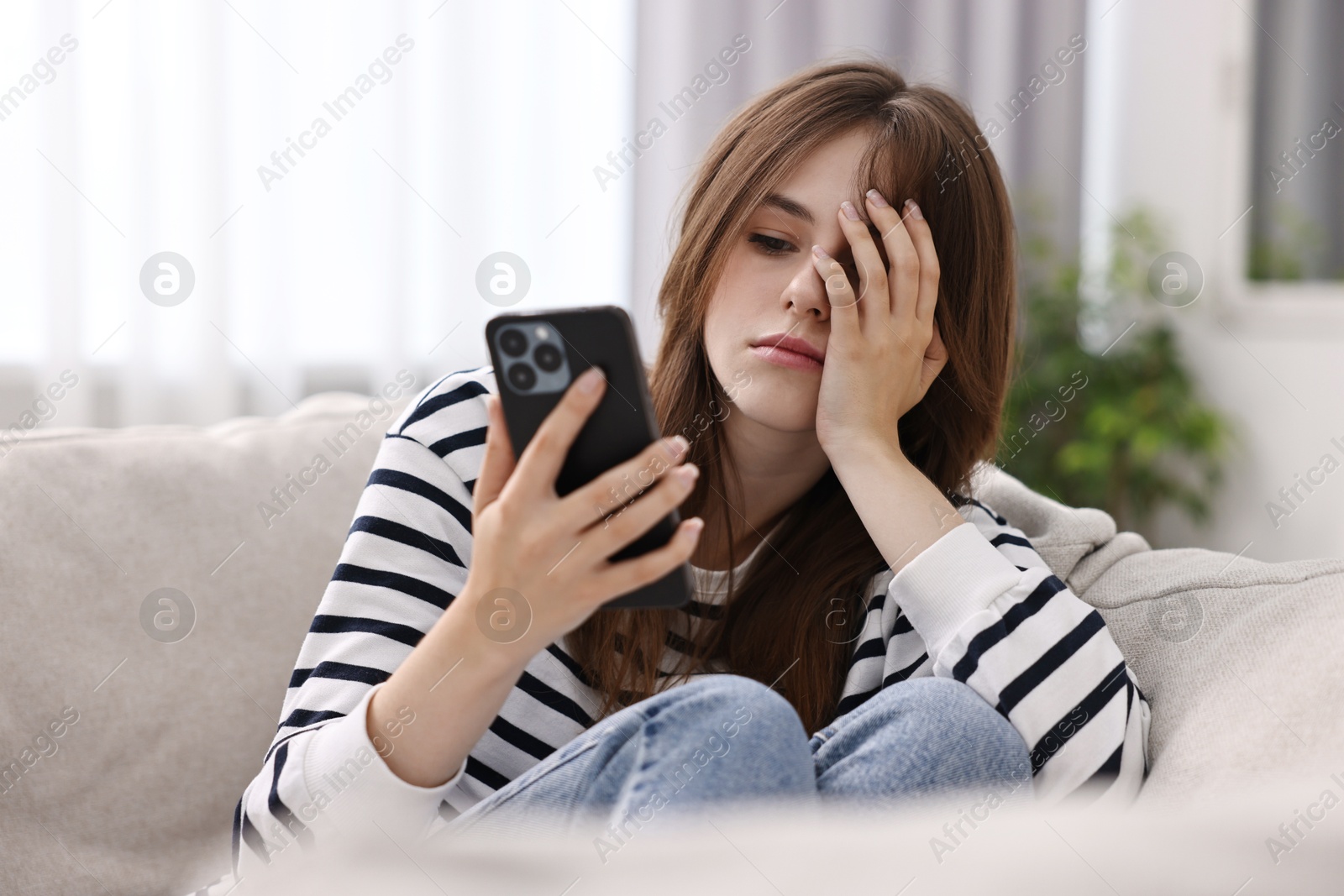 Photo of Loneliness concept. Sad teenage girl using smartphone on sofa at home