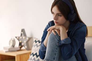 Photo of Loneliness concept. Sad teenage girl in headphones listening to music on bed at home