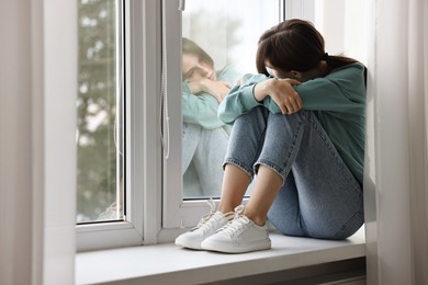 Loneliness concept. Sad teenage girl on windowsill at home