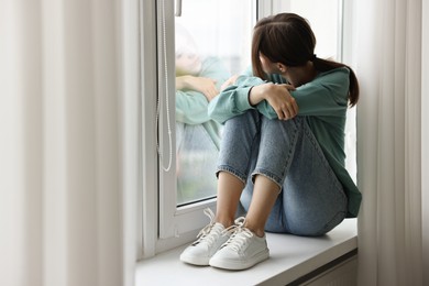 Loneliness concept. Sad teenage girl on windowsill at home