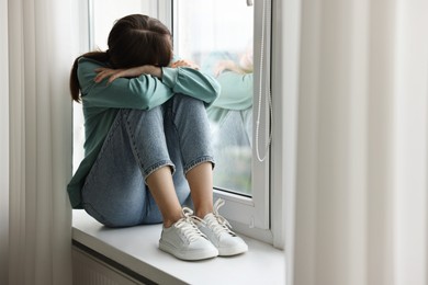 Photo of Loneliness concept. Sad teenage girl on windowsill at home