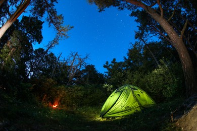 Photo of Modern camping tent and bonfire in forest at night. Fisheye lens effect