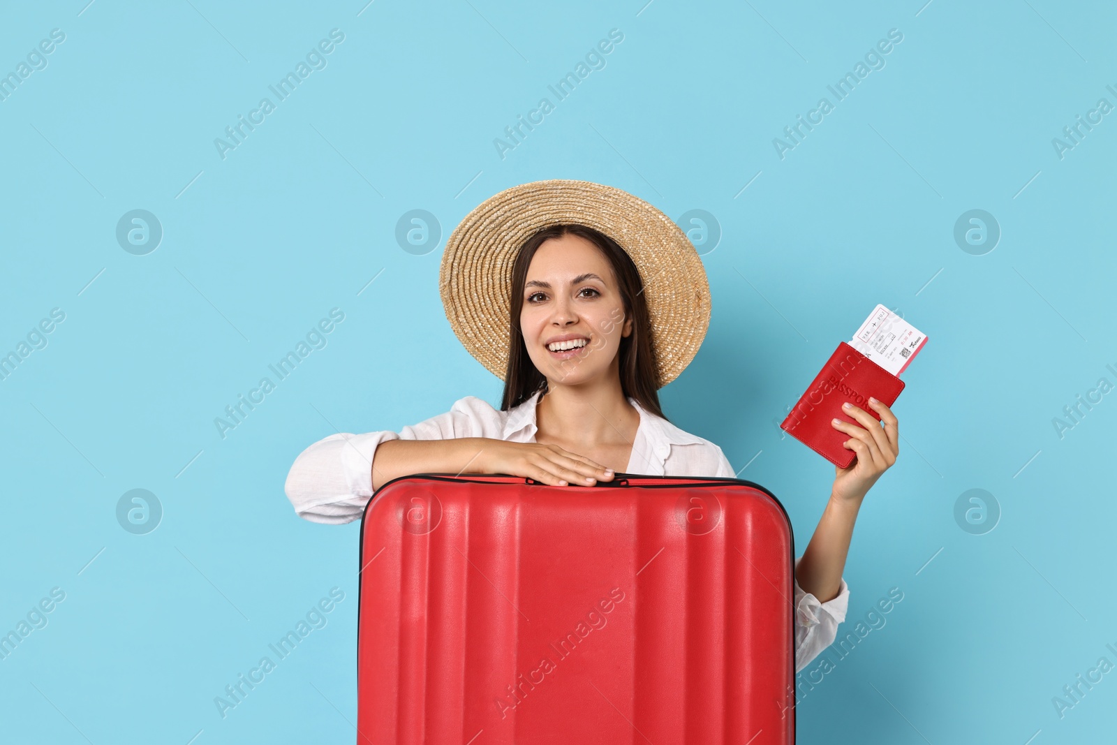 Photo of Happy young woman with suitcase, passport and ticket on light blue background