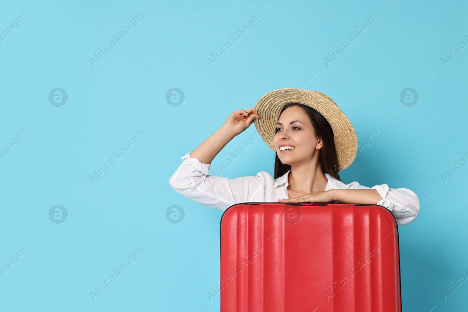 Photo of Happy young woman with suitcase on light blue background, space for text